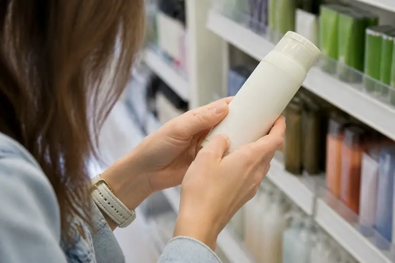 Main féminine examinant avec soin la liste des ingrédients sur l'étiquette d'un produit cosmétique.