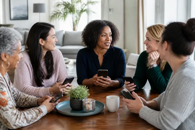 Un groupe de femmes discute en partageant leurs avis sur des produits cosmétiques consultés sur leurs téléphones.