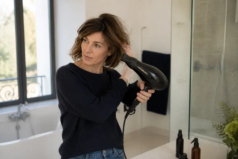 Une femme française sèche ses cheveux avec un sèche-cheveux pour donner du mouvement à son carré dégradé, utilisant des produits coiffants.
