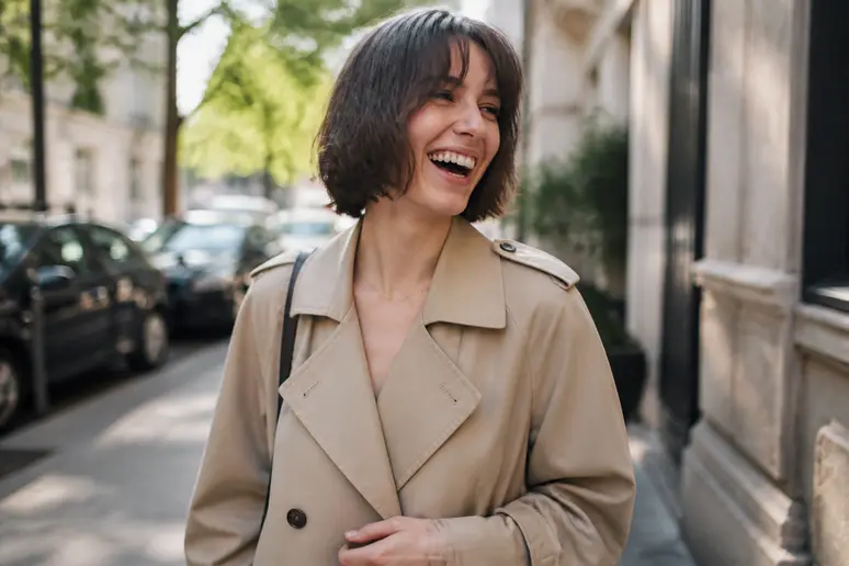 Une Parisienne souriante arbore un bob texturé tendance avec une frange rideau, dans une rue ensoleillée.