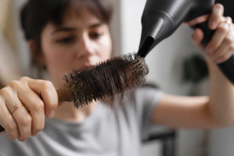 Des mains expertes coiffent une frange courte avec un sèche-cheveux et une brosse ronde pour un style impeccable.