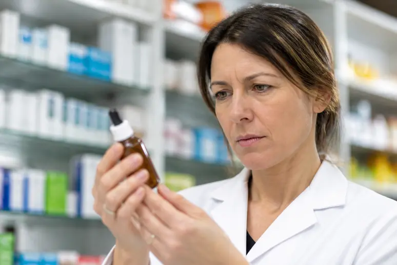 Un pharmacien français examine attentivement une petite bouteille de Fleurs de Bach Florna dans une officine.