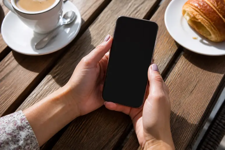 Mains d'une consommatrice tenant un smartphone affichant des avis sur Florna Fleurs de Bach dans un café parisien.