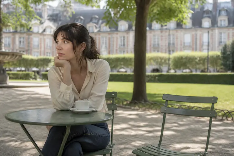 Une femme française songeuse assise seule à une terrasse de café parisien, réfléchissant au comportement d'un homme-trop-etouffant.