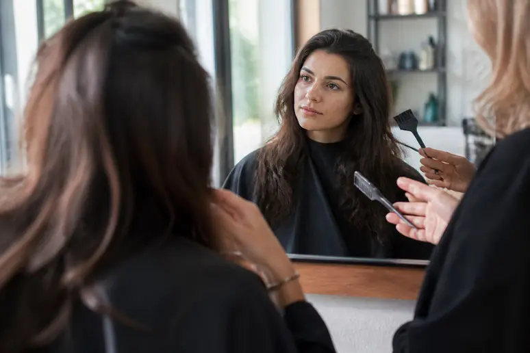 Une femme aux cheveux châtain foncé discute des nuances miel et caramel avec son coiffeur dans un salon lumineux et moderne.