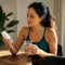 Femme tenant un flacon de complément alimentaire et un verre d'eau pour consulter un Vinali avis.