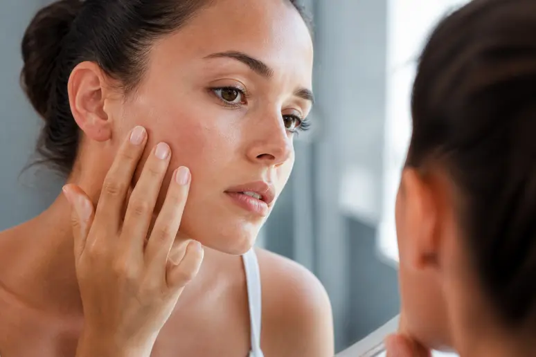 Femme examinant son profil cutané propre et naturel devant un miroir pour choisir ses soins.