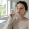 Une femme en pull beige tient un flacon en verre pour illustrer comment choisir ses soins au quotidien.