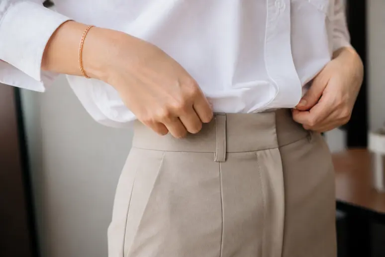 Mains rentrant le devant d'une chemise dans un pantalon taille haute pour ajuster ses tenues au quotidien