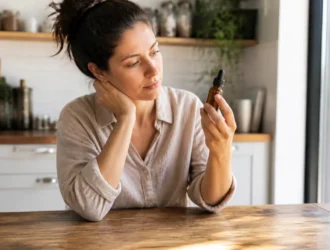 Une femme examine un flacon d'huile cosmétique dans sa cuisine, illustrant un vitalis cheveux avis négatif.