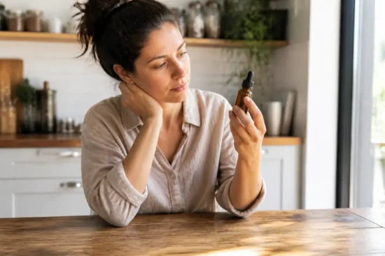 Une femme examine un flacon d'huile cosmétique dans sa cuisine, illustrant un vitalis cheveux avis négatif.