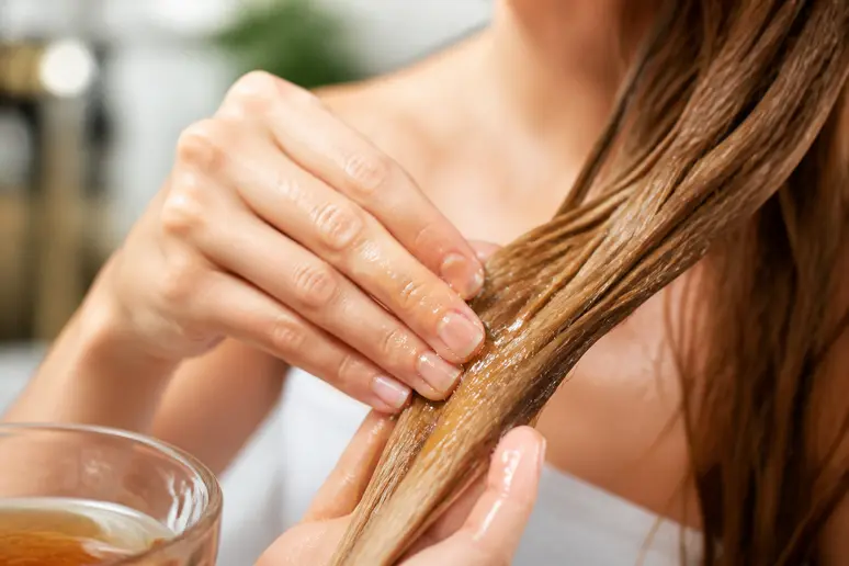 Application d'un soin végétal nourrissant sur des mèches de cheveux clairs pour obtenir un éclaircissement naturel.