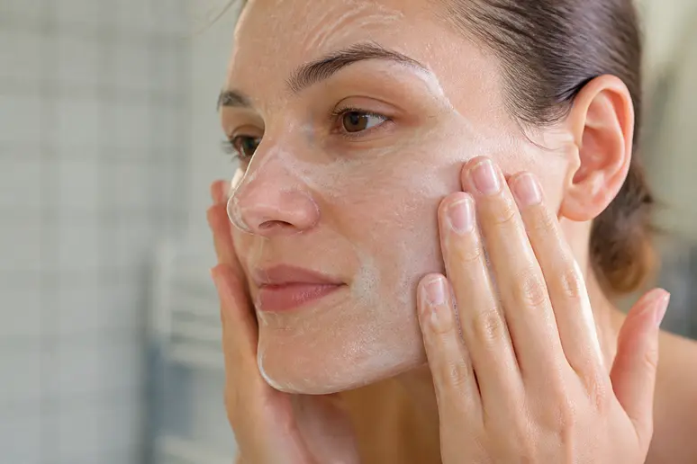 Mains nettoyant délicatement le visage avec un soin doux pour optimiser la routine skincare.