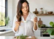 Une femme tient un pot d'huile de coco pour la peau dans sa cuisine lumineuse.