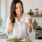 Une femme tient un pot d'huile de coco pour la peau dans sa cuisine lumineuse.