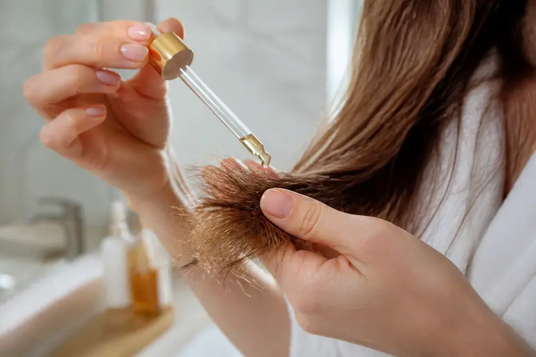 Application de soins capillaires nourrissants à l'aide d'une pipette sur les longueurs.