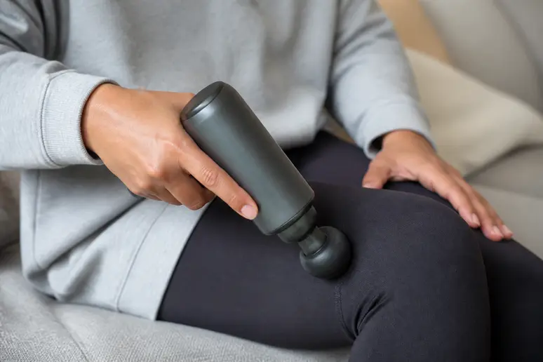 Utilisation d'un masseur électrique sur une jambe vêtue d'un pantalon