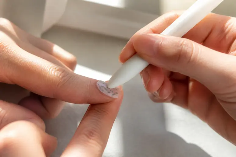 Lissage minutieux d'un sticker pour ongles avec un embout en silicone pour chasser l'air